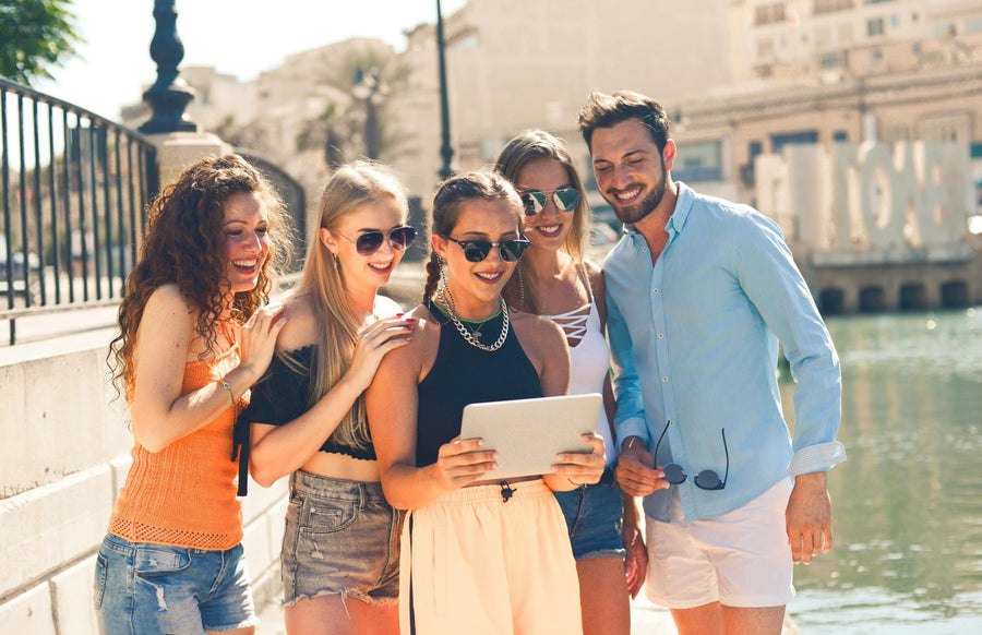 Trendy young adults in casual summer clothing smiling and looking at a tablet outdoors